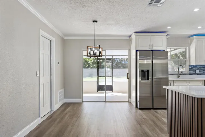 Dining Nook &amp; Patio Access: Light-filled dining area featuring a modern lantern chandelier, sliding glass door access to the screened patio, and view into the kitchen.