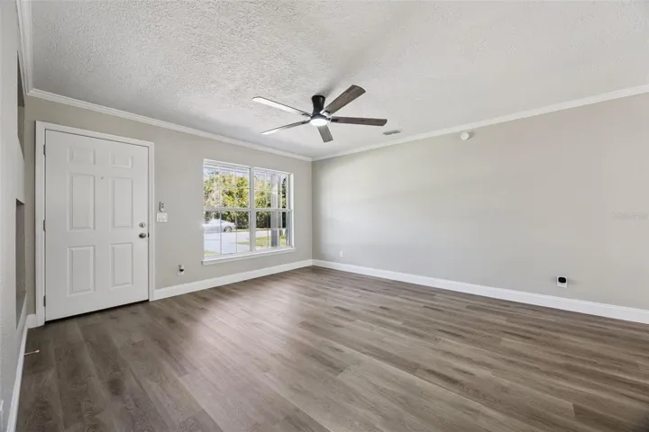 Foyer &amp; Living Area: Welcoming front foyer and open living room featuring luxury vinyl plank flooring, neutral paint, crown molding, and a modern ceiling fan