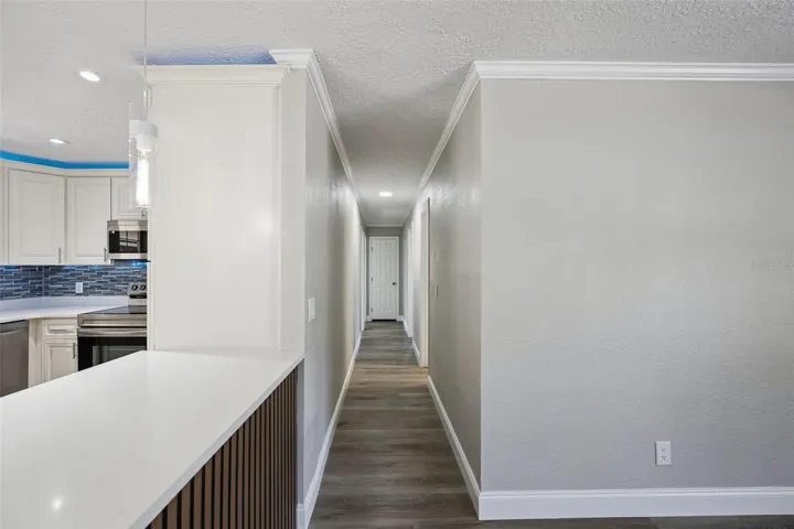 Central Hallway Corridor: Bright central hallway with luxury vinyl plank flooring, neutral paint, crown molding, and view past the custom slatted kitchen peninsula