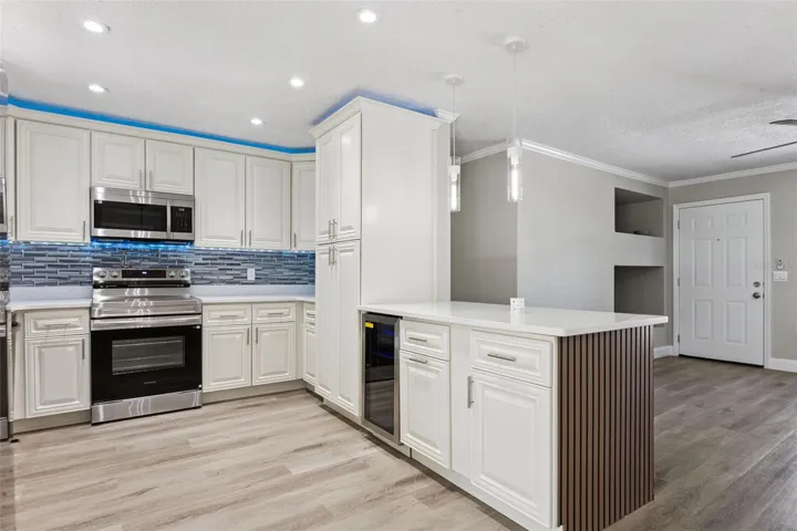 Gourmet Kitchen Overview: Upgraded kitchen featuring white raised-panel cabinets, stainless steel appliances, a mosaic tile backsplash, and a breakfast bar peninsula.
