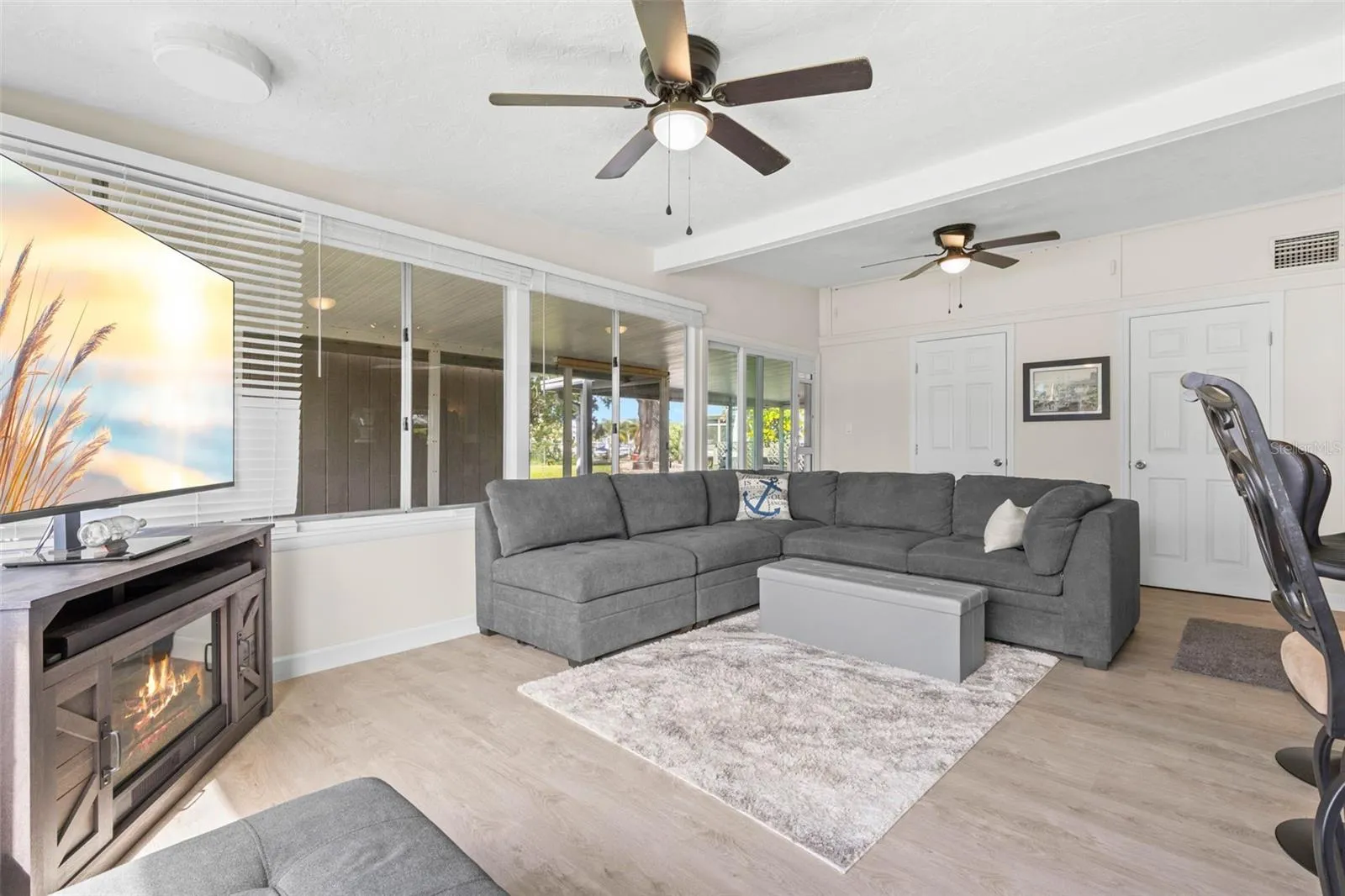 The spacious living room offers dual ceiling fans, luxury vinyl plank flooring, (2025) and a cozy fireplace, while a wall of windows and glass doors brings in abundant natural light and extends the view toward the screened porch and backyard.