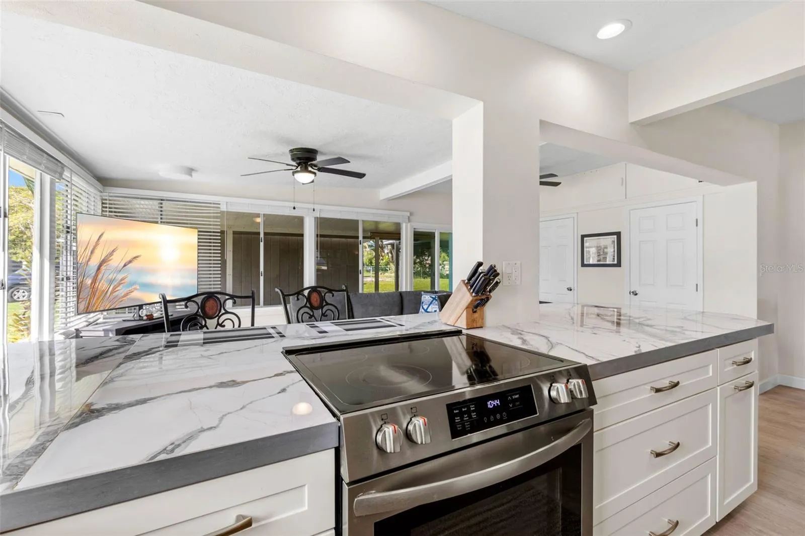 The updated kitchen (2025) showcases dramatic stone-look countertops, white Shaker-style cabinetry, stainless steel appliances, recessed lighting, and generous drawer storage, with an open design that keeps the cook connected to the adjoining living space.