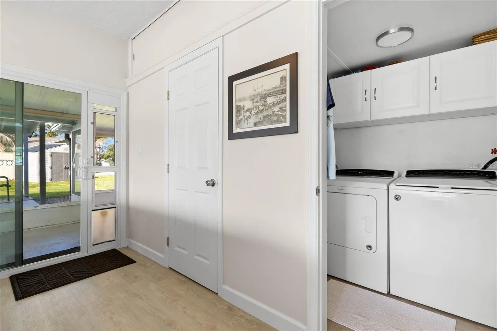 A dedicated laundry room keeps everyday chores tucked neatly away, with a full-size washer and dryer, overhead cabinetry for storage, and convenient access to the screened lanai and backyard.