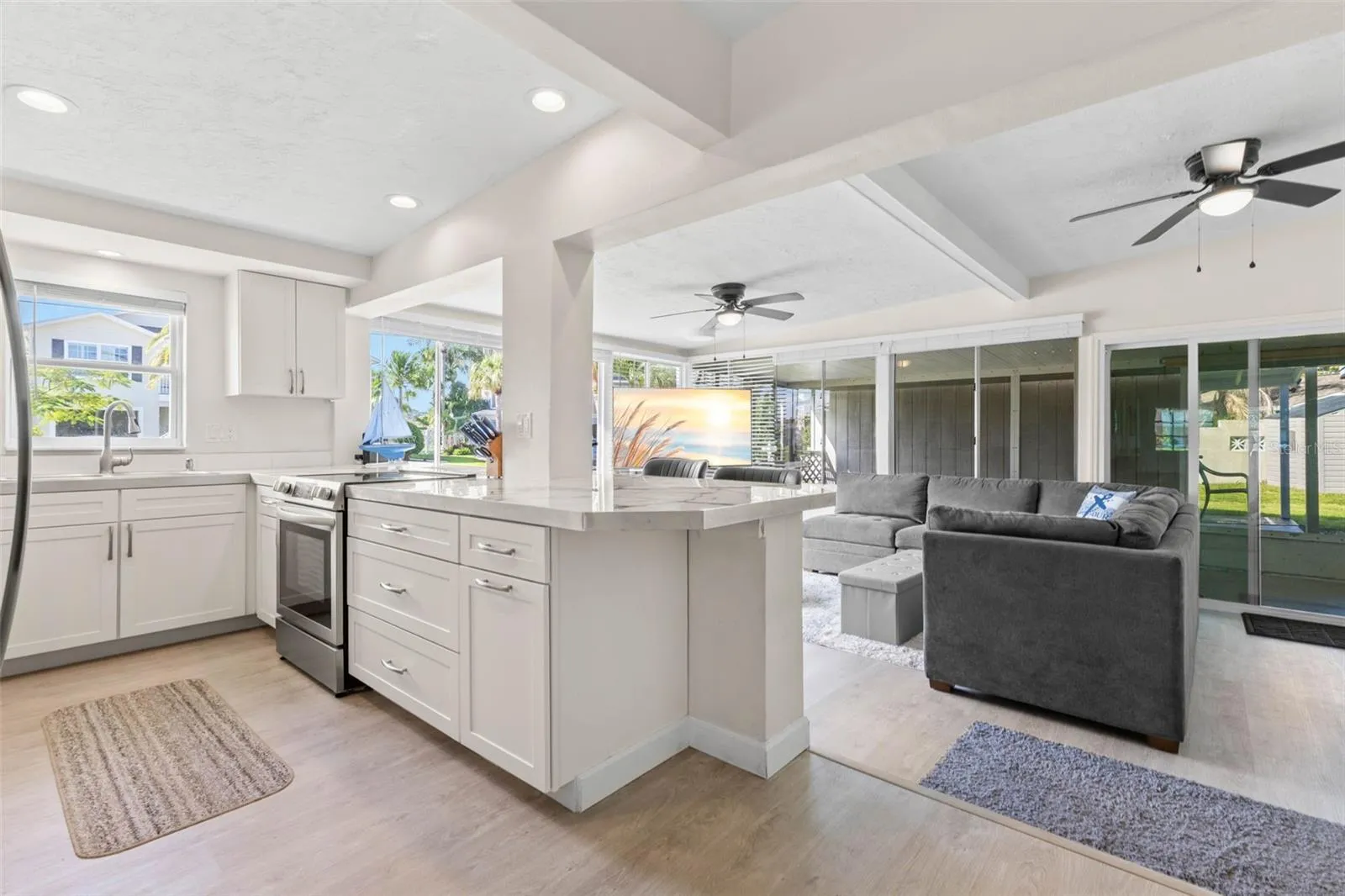 The updated kitchen (2025) opens directly to the living area and features crisp white cabinetry, stainless steel appliances, abundant counter space, recessed lighting, and a generous breakfast bar for casual seating or serving.