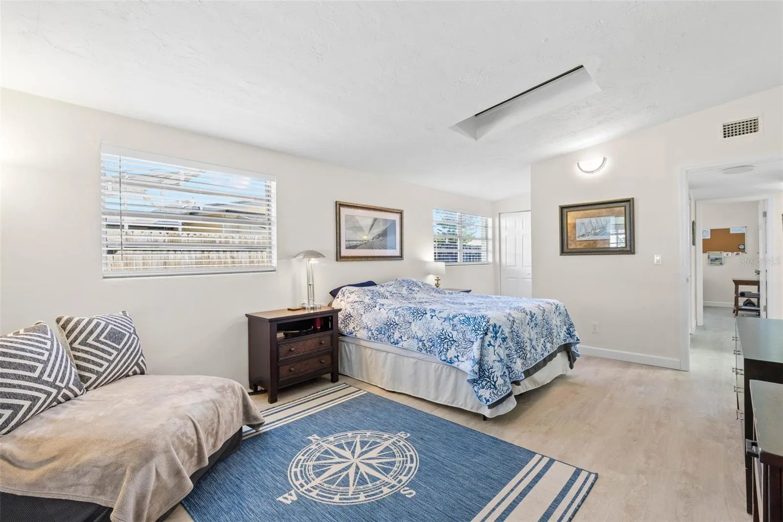 The spacious primary bedroom easily accommodates a king-size bed and a dedicated sitting area, with multiple windows, a skylight, neutral tones, and luxury vinyl plank flooring (2025) adding to the bright, open feel.