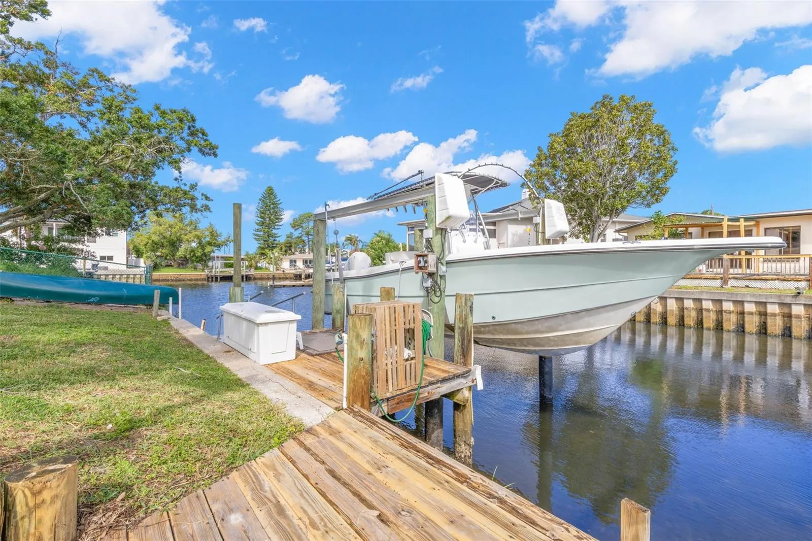 The waterfront setup is ready for serious boating, with a substantial wooden dock, 10,000-pound boat lift with davits, waterside storage, and a convenient water connection—all directly on the canal with access toward the Gulf.