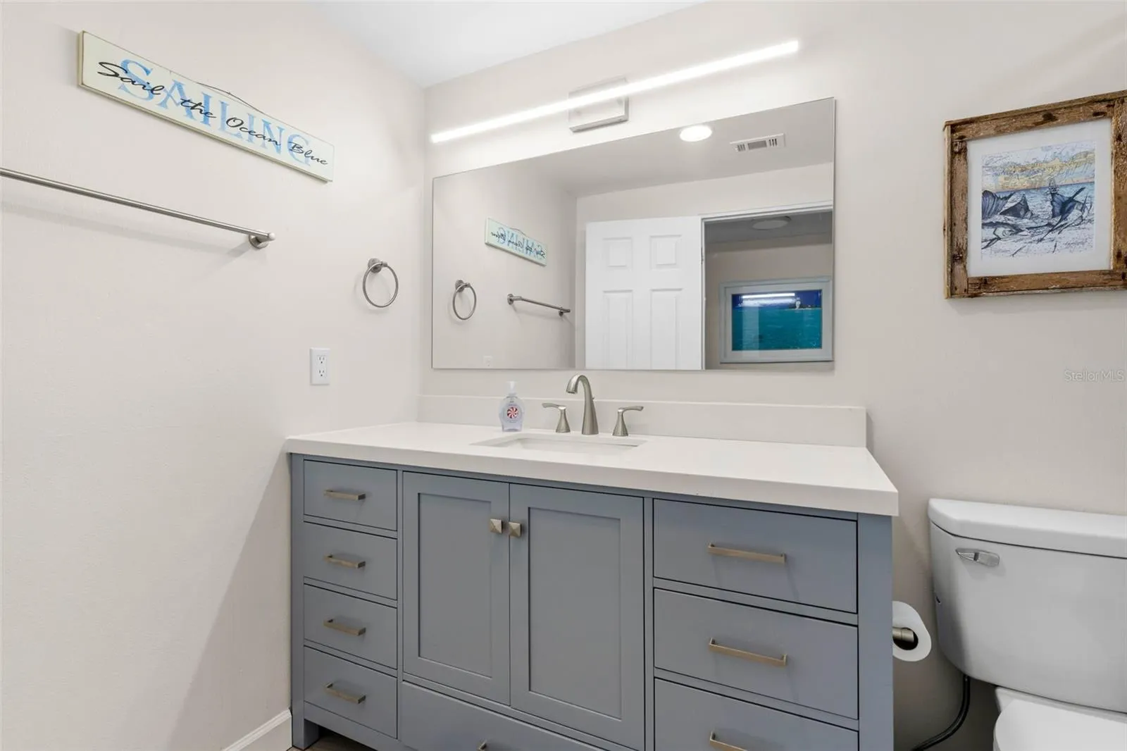 The remodeled primary bath (2025) features a wide gray vanity with abundant drawer storage, a sleek white countertop, oversized mirror, and contemporary linear lighting.