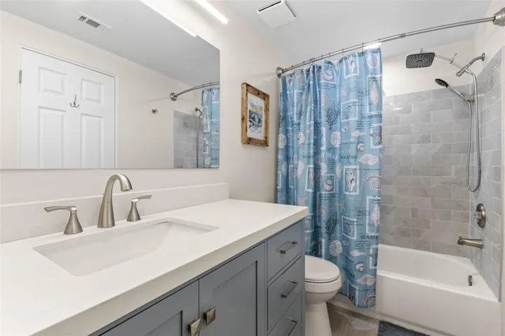 The remodeled primary bath (2025) pairs a wide gray vanity and sleek white countertop with a tiled tub/shower surround, rainfall showerhead, handheld sprayer, and updated fixtures for a clean, modern finish.