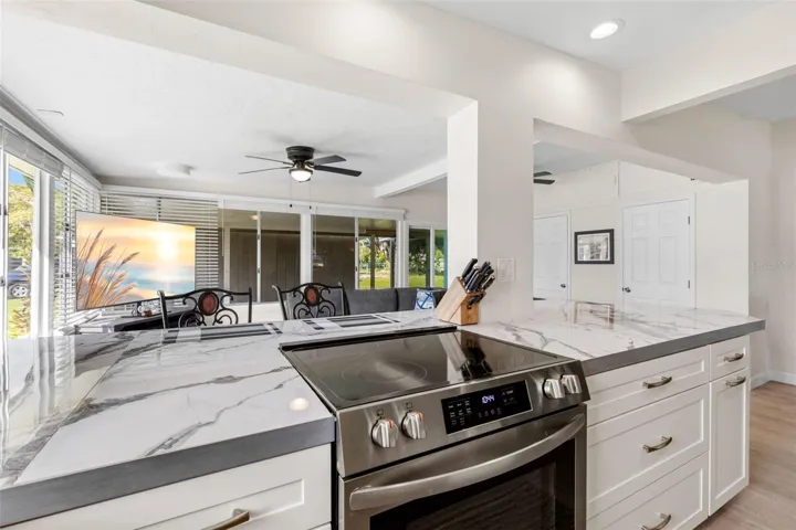 The updated kitchen (2025) showcases dramatic stone-look countertops, white Shaker-style cabinetry, stainless steel appliances, recessed lighting, and generous drawer storage, with an open design that keeps the cook connected to the adjoining living space.