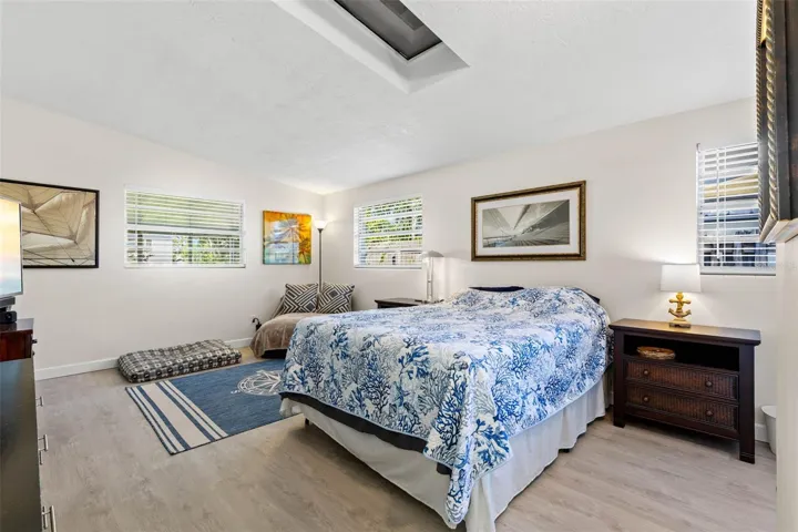 The generously sized primary bedroom feels bright and airy with multiple windows, a skylight overhead, neutral tones, and luxury vinyl plank flooring (2025), plus plenty of room for a sitting area in addition to a king-size bed.