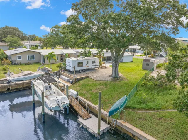 An aerial view showcases the property’s waterfront lifestyle, with a 10,000-pound boat lift, wooden dock and floating dock along the canal, plus generous lawn space, RV parking, and mature shade trees just steps from the water.