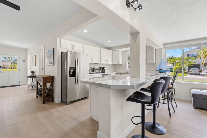 The updated kitchen (2025) pairs crisp white cabinetry and stainless steel appliances with expansive counter space and a wraparound breakfast bar that adds both seating and everyday functionality.