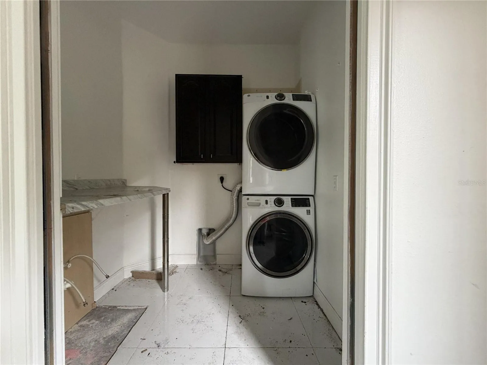 Laundry room with stacked appliances; utility sink and lower cabinetry removed.