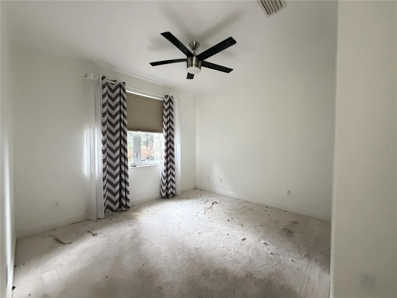 Secondary bedroom with ceiling fan, window, and heavily stained carpet.