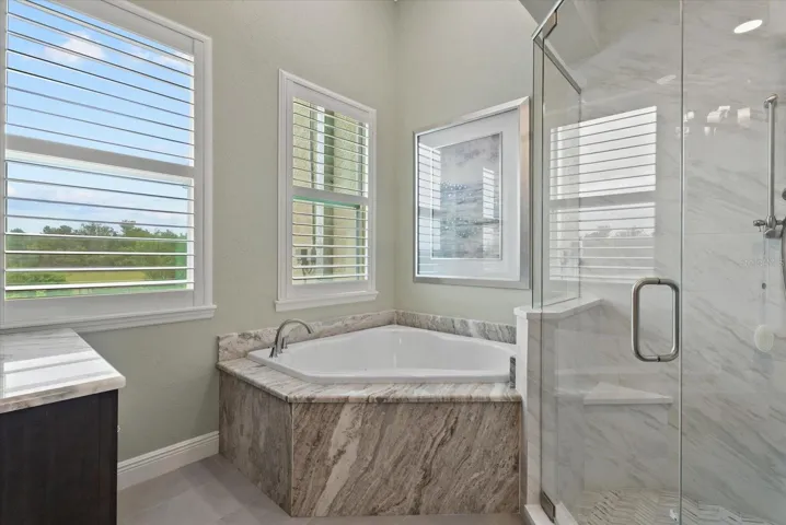 A step in shower and deep garden tub are tucked into the corner of the ensuite bath of the primary suite