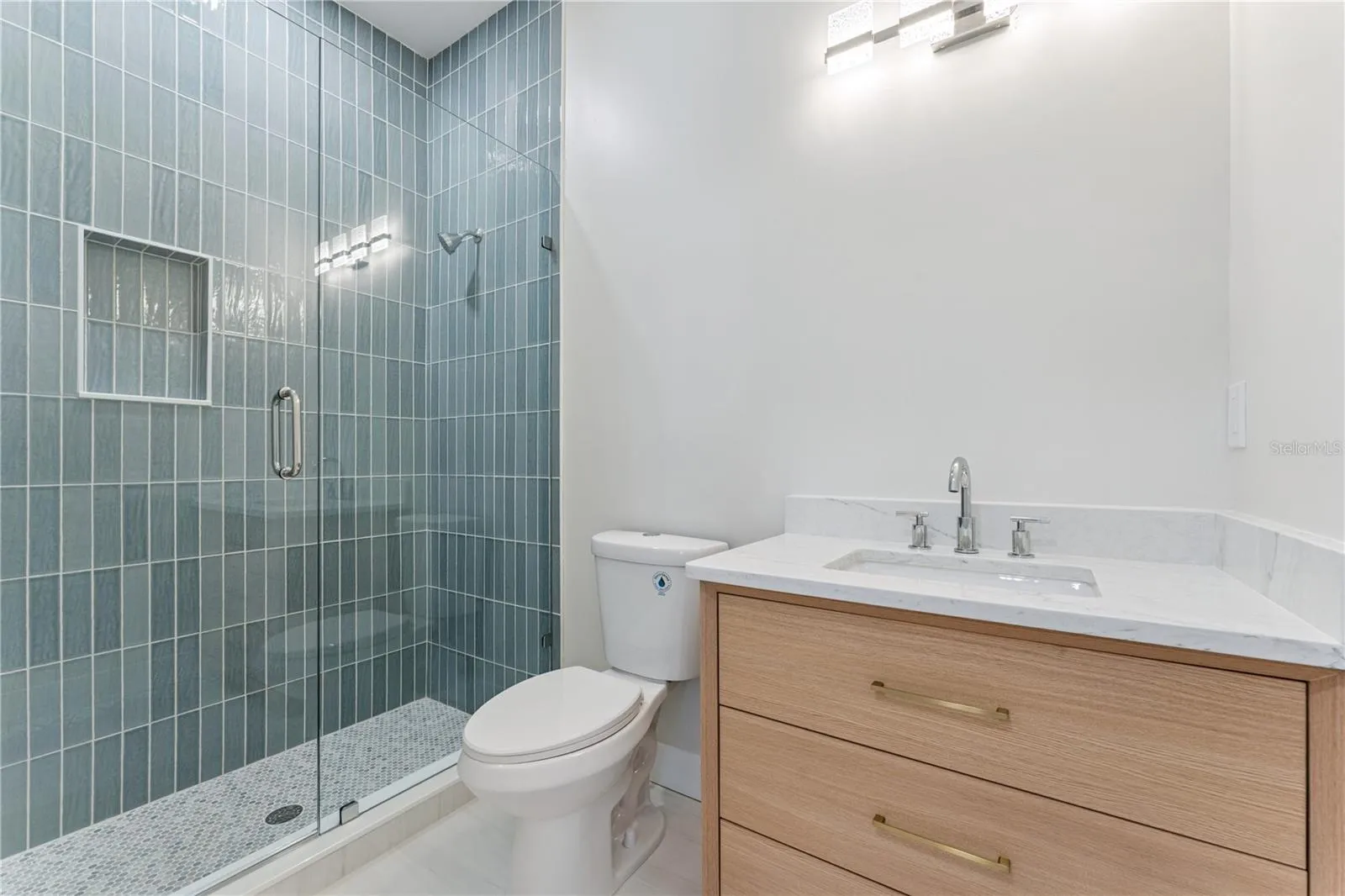 Blue shower tile and a wood-toned vanity add color and warmth to this bathroom.