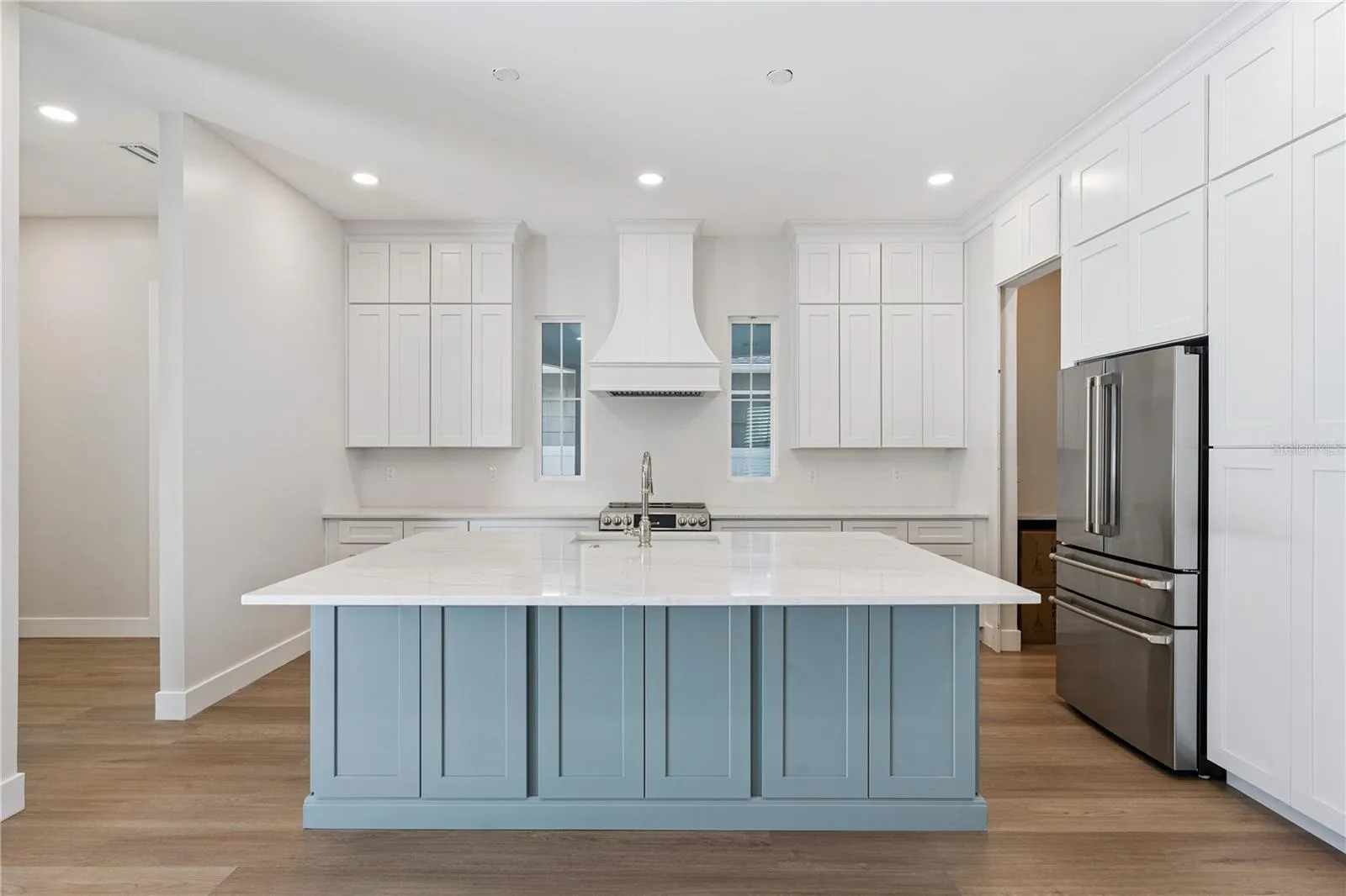 Main kitchen at 3456 Fairway Ln with a blue island, white counters, range hood, and stainless steel appliances.
