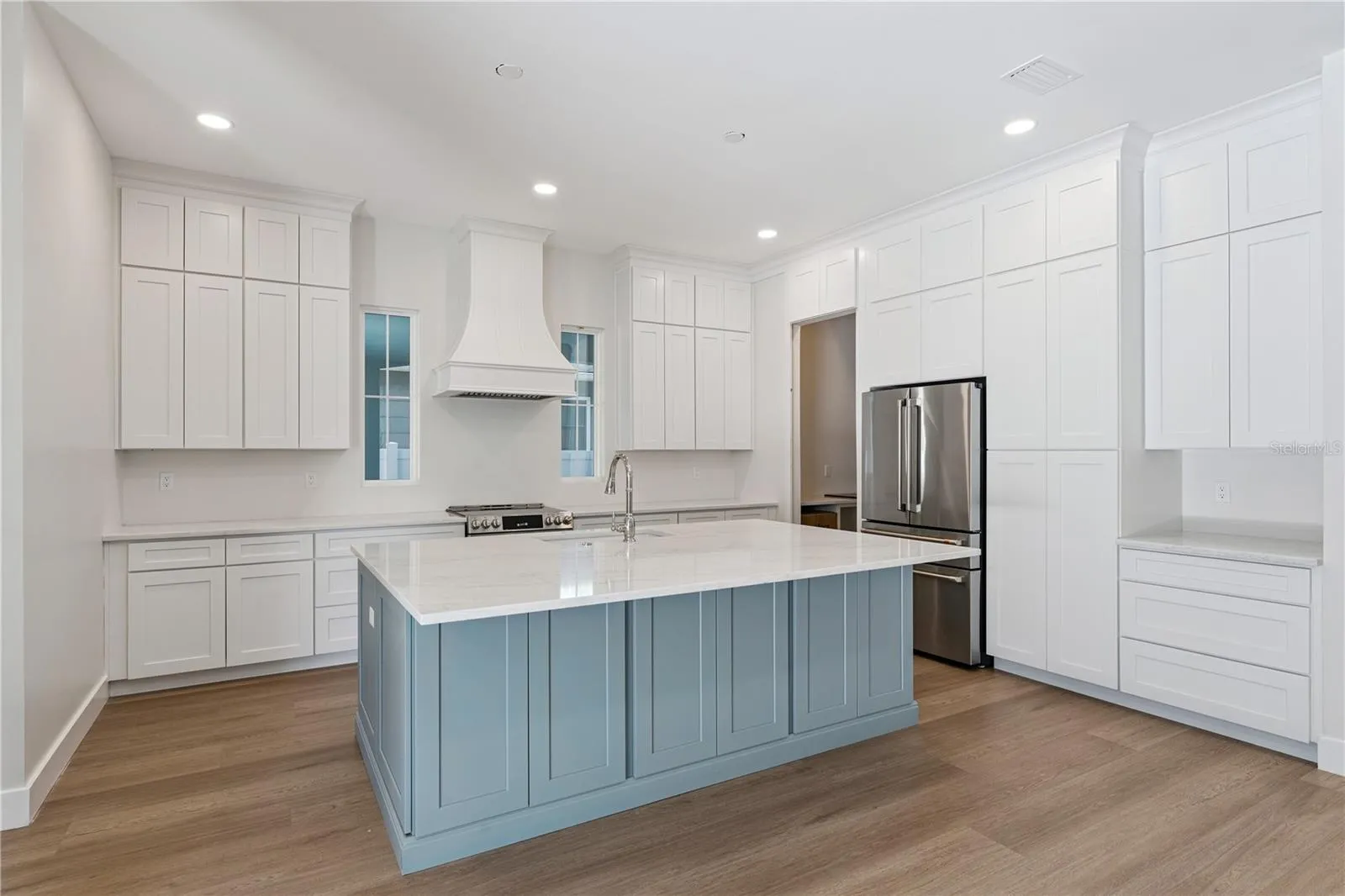 The main kitchen features a blue island, white cabinetry, a statement range hood, and stainless steel appliances.