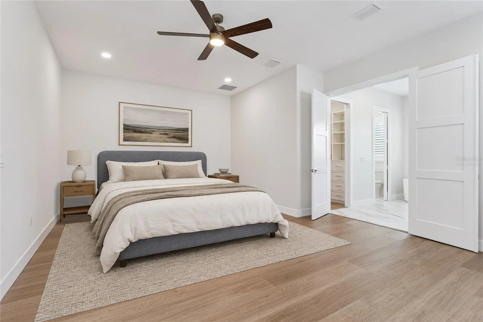 Virtually Staged - The primary bedroom features a ceiling fan and a view toward the adjoining bathroom.