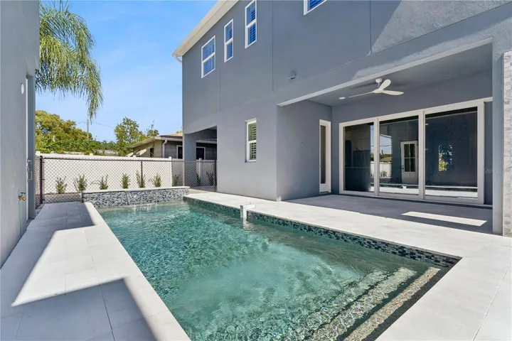 The pool sits beside a paved deck and covered rear patio, creating an inviting outdoor setting.