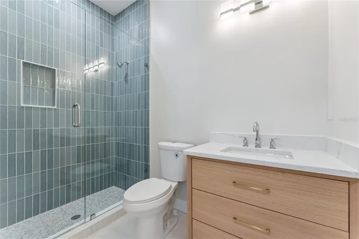 Blue shower tile and a wood-toned vanity add color and warmth to this bathroom.