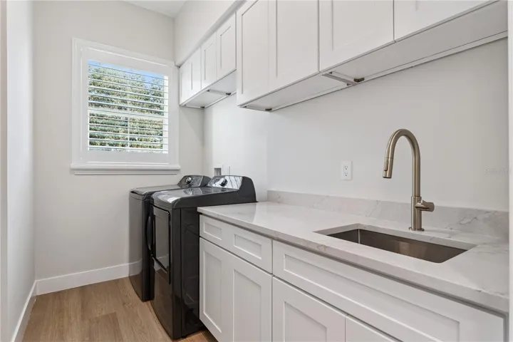 The laundry room includes a washer, dryer, utility sink, and upper and lower cabinetry.