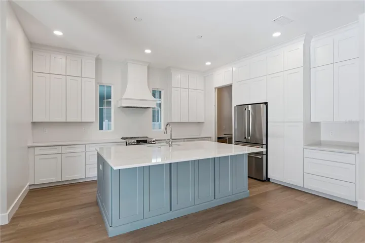 The main kitchen features a blue island, white cabinetry, a statement range hood, and stainless steel appliances.
