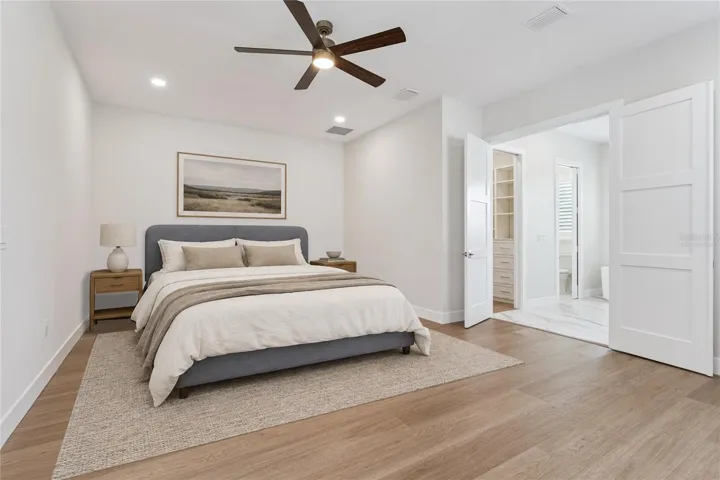 Virtually Staged - The primary bedroom features a ceiling fan and a view toward the adjoining bathroom.