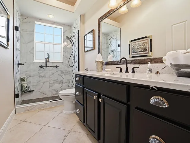 LOVELY RENOVATED GUEST BATH WITH FRAMELESS GLASS DOOR TO THE TILED SHOWER, QUARTZ COUNTERS FRAMED MIRROR AND NEW LIGHT FIXTURE.  ALL OF THE TOILETS IN THE HOME ARE ALL A NEW TALLER STYLE.