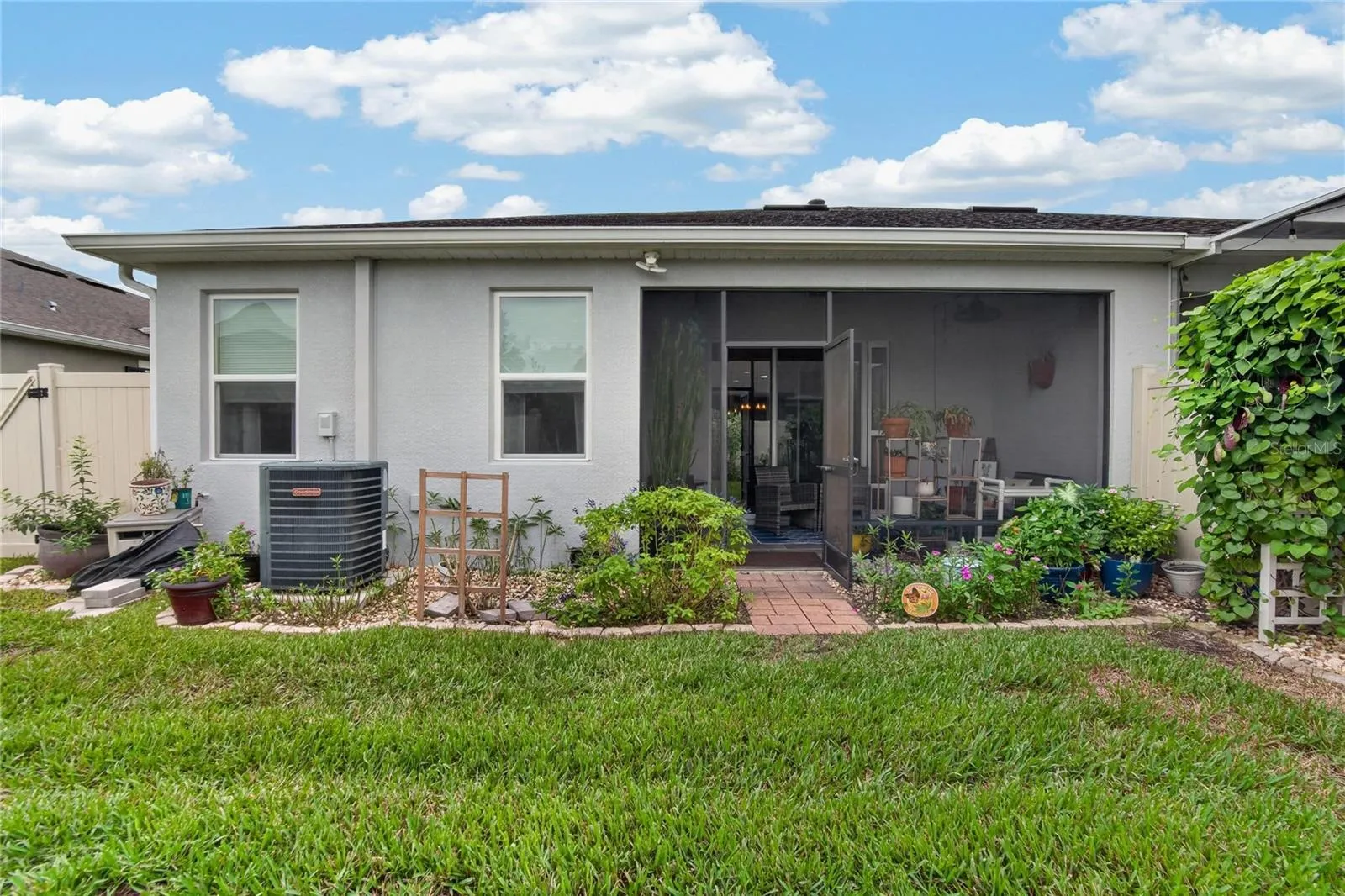The rear exterior shows the screened lanai, landscaped beds and direct connection to the fenced backyard