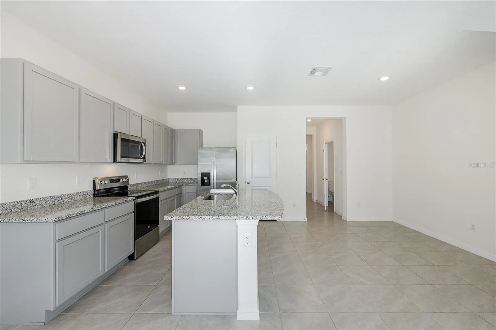Modern, open-concept kitchen featuring granite countertops, stainless-steel appliances, gray cabinetry and a spacious center island