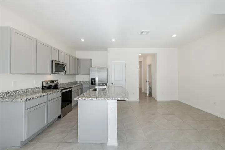 Modern, open-concept kitchen featuring granite countertops, stainless-steel appliances, gray cabinetry and a spacious center island
