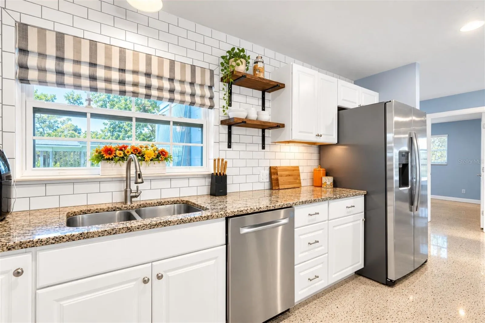 Convenient pass-through window connects the kitchen to the patio. Free floating shelves add character to the farmhouse kitchen.