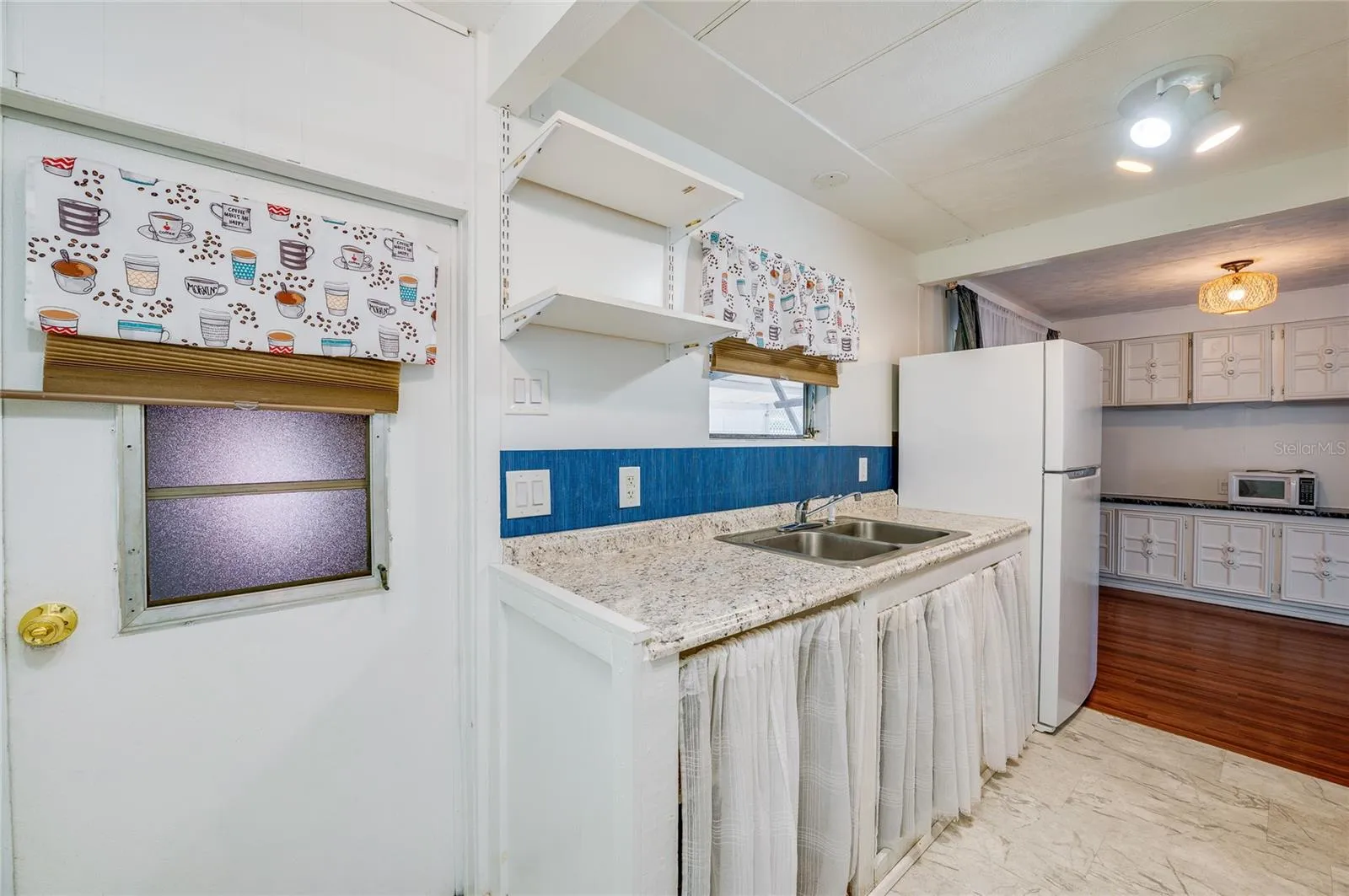 Additional kitchen view showcases the long countertop and sink area, open shelving, and convenient connection to the adjacent dining space.