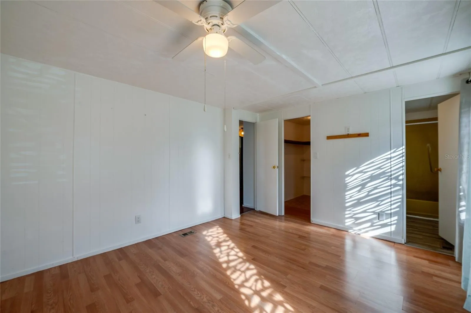 Additional view highlights the room’s open floor area, ceiling fan, and convenient access to a walk-in closet and adjoining bathroom.