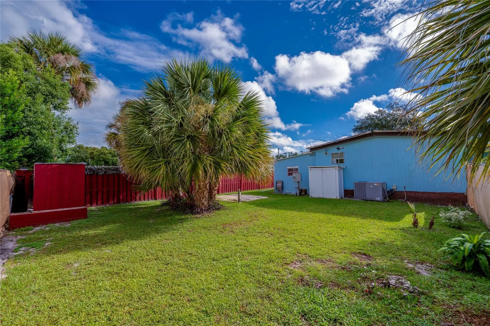 Rear view highlights the generous lawn, established tropical landscaping, and exterior access along the back of the home.