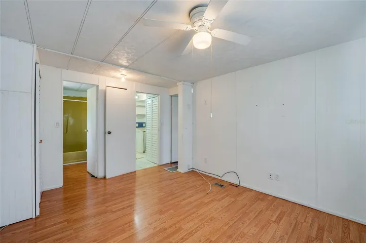 Another view highlights the room’s generous open floor area, ceiling fan, and convenient access to the adjoining bath and nearby living spaces.