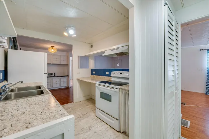 Functional eat-in kitchen features generous counter space, a double-basin sink, range with hood, refrigerator, and a pass-through opening that connects with the adjoining living area.