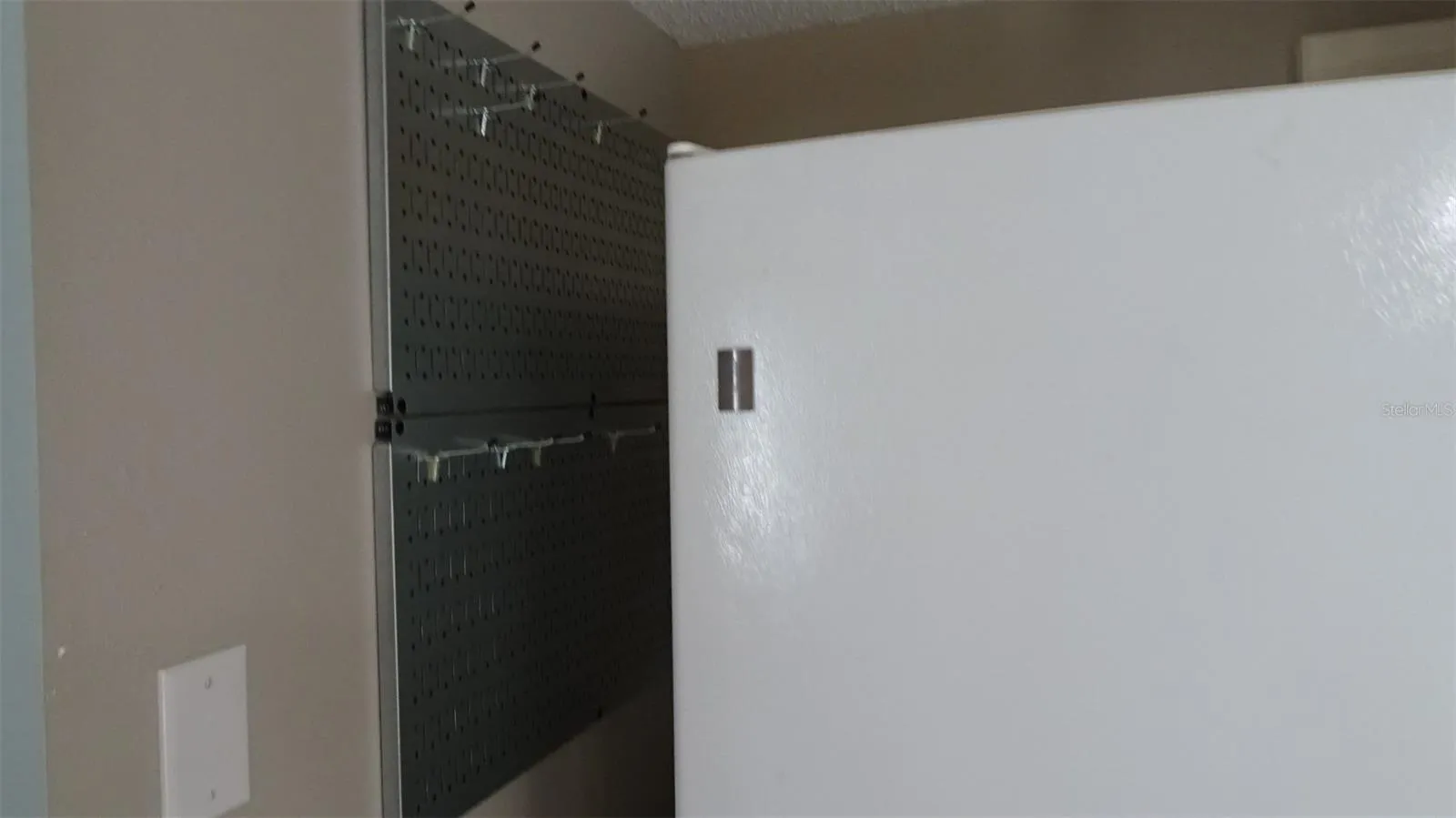 Pegboard with hooks next to refrigerator for pots and pans and whatnots.