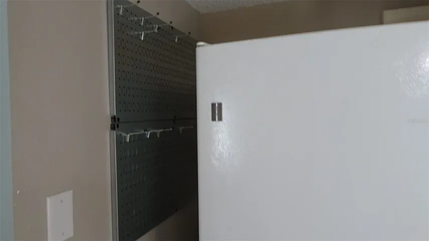 Pegboard with hooks next to refrigerator for pots and pans and whatnots.