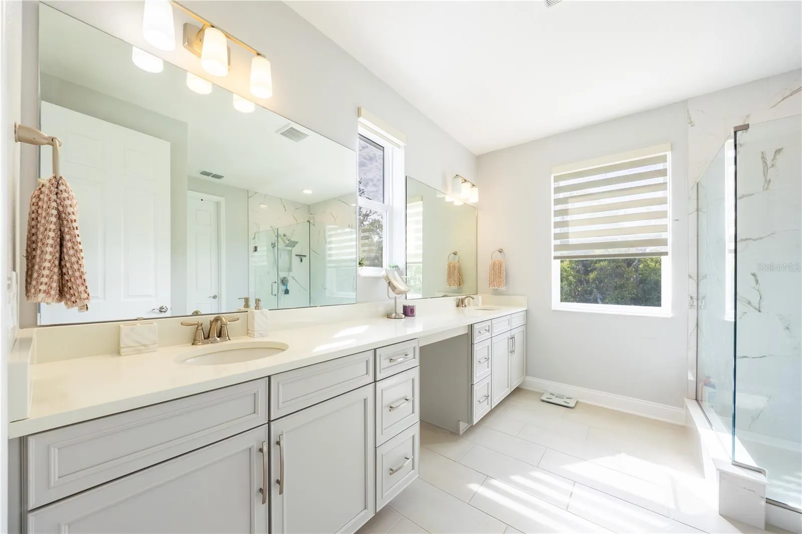 Elegant bathroom with a dual-sink vanity, dressing area, and glass-enclosed shower.