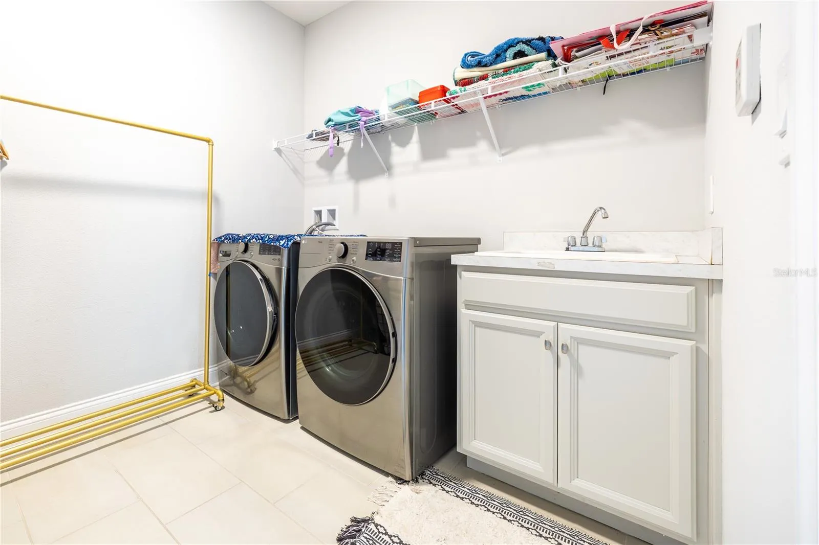 Laundry room with included front-load washer and dryer, utility sink, and storage shelving.