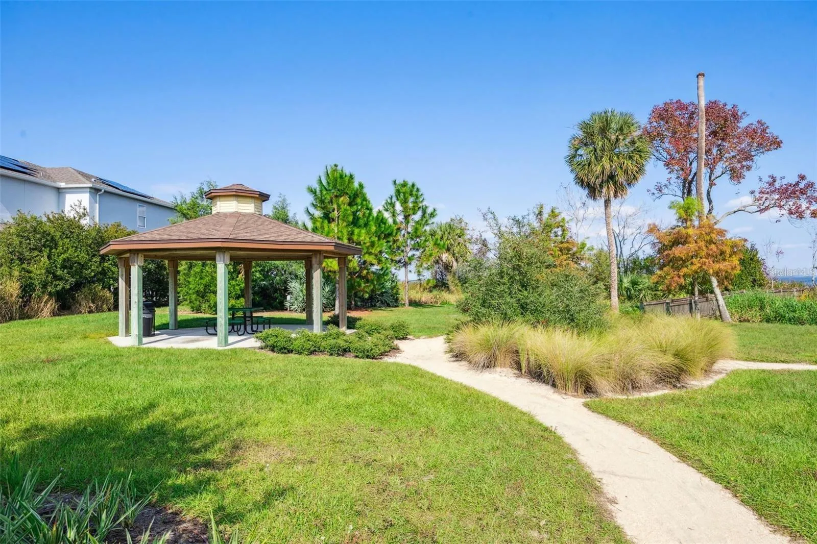 Covered picnic pavilion surrounded by lush landscaping, with a walking path leading toward the lake.