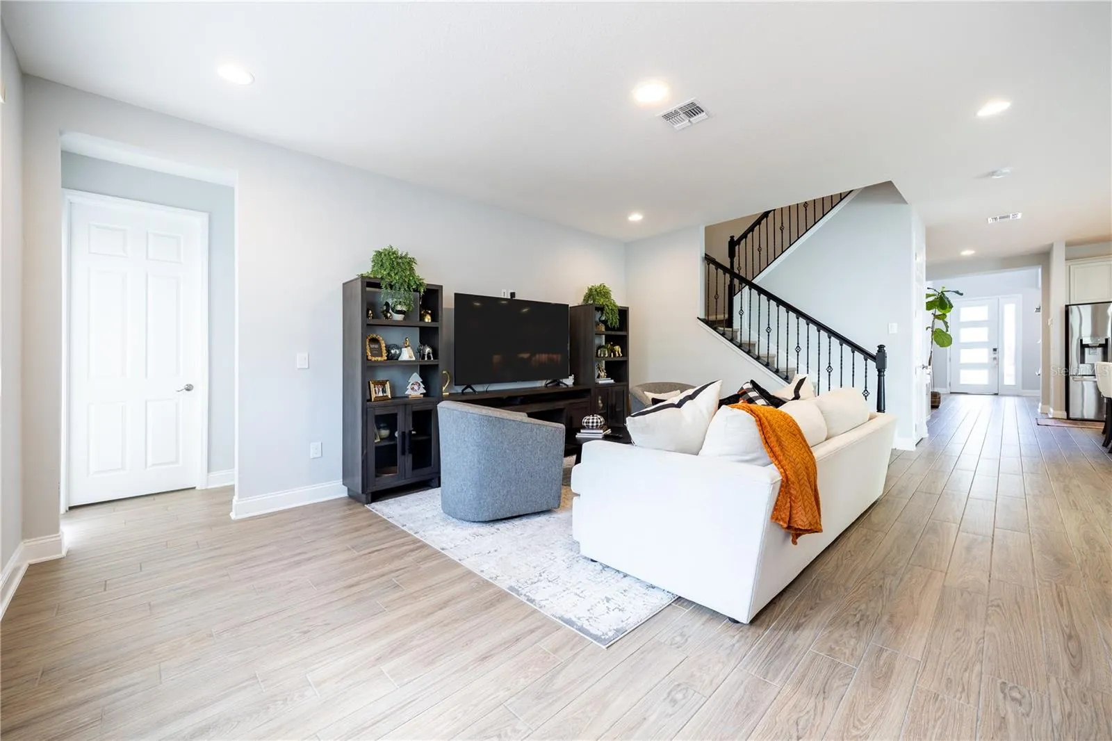 Open-concept living room with wood-look tile flooring and a staircase with decorative metal railings.