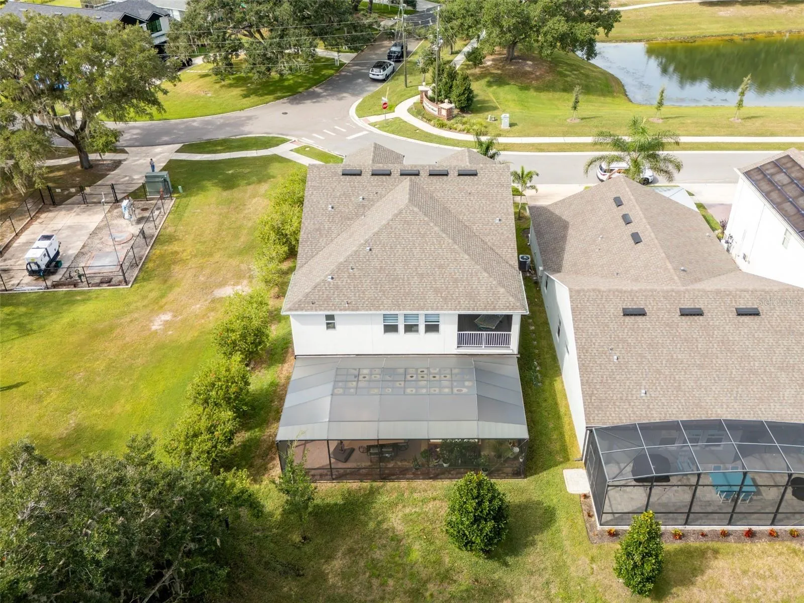 Rear aerial view showcasing an expansive screened patio, covered upstairs balcony, and wooded surroundings.
