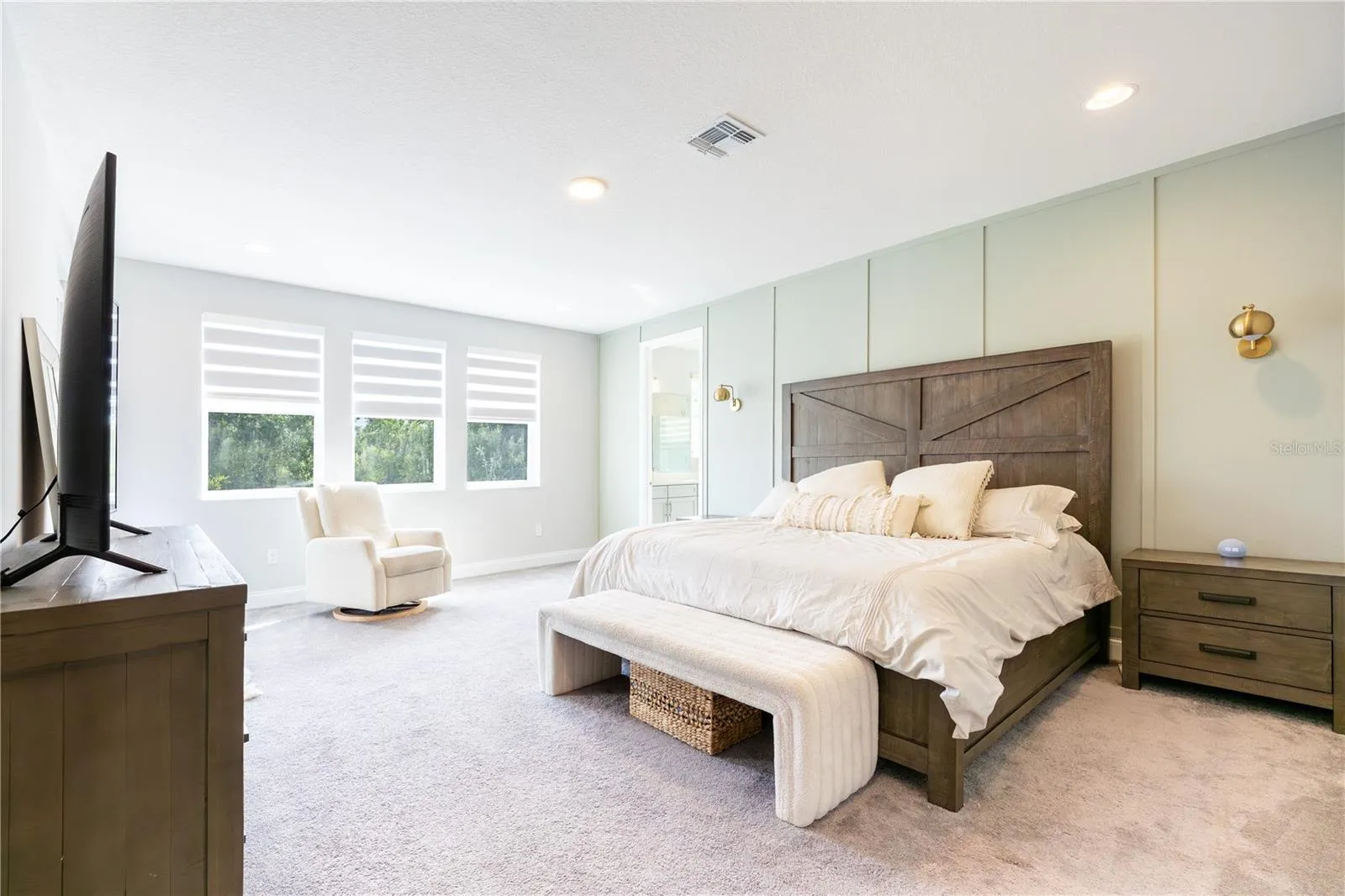 Spacious primary bedroom with an elegant accent wall, sitting area, and porch access with views of a conservation area.