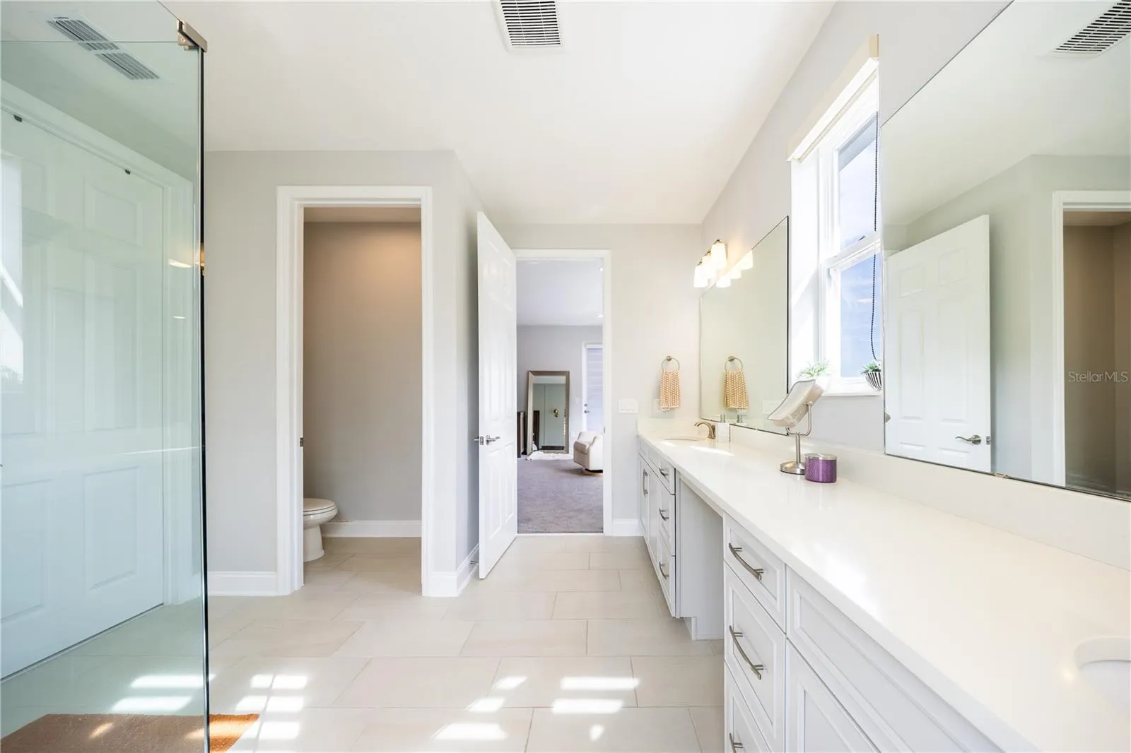 Elegant primary bathroom with an expansive vanity, makeup area, and separate toilet room.