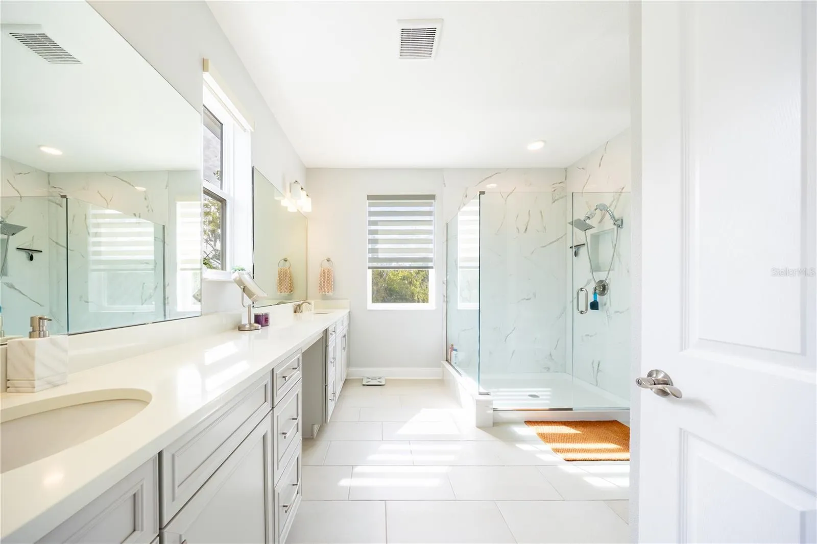 Spacious primary bathroom with a dual-sink vanity, makeup area, and frameless glass shower.
