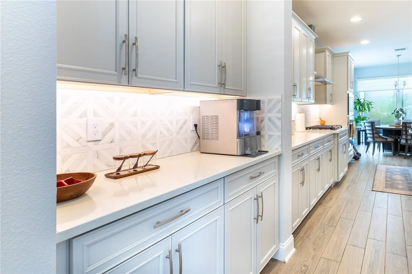Stylish serving area with white cabinetry, geometric tile backsplash, and under-cabinet lighting.