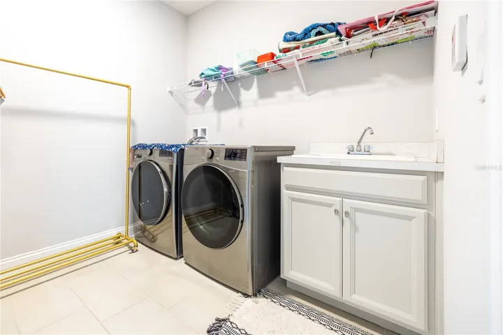 Laundry room with included front-load washer and dryer, utility sink, and storage shelving.